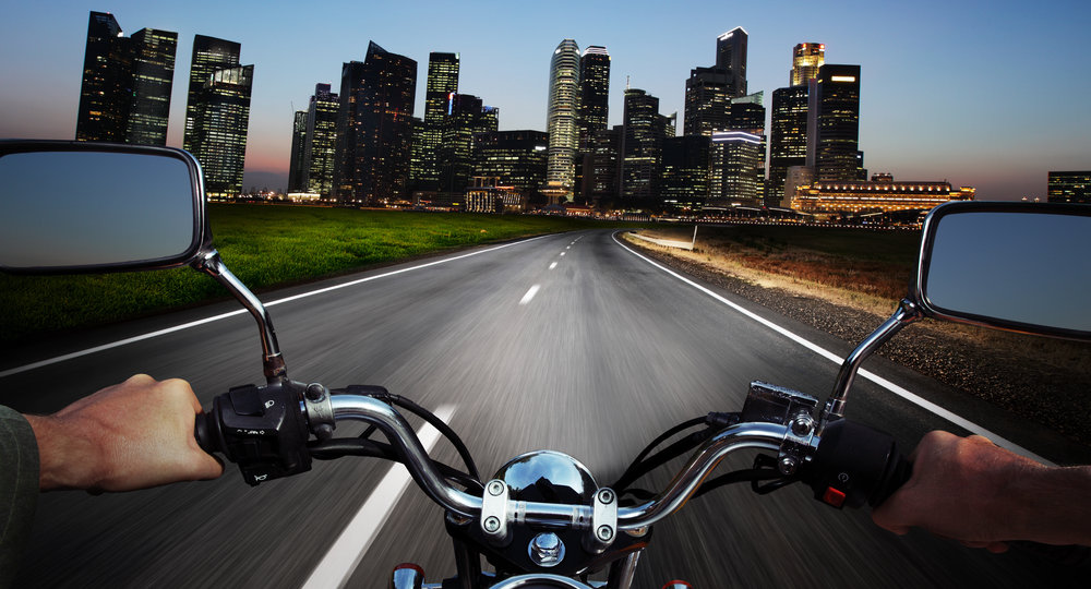 Driver riding motorcycle on an asphalt road at night towards big city